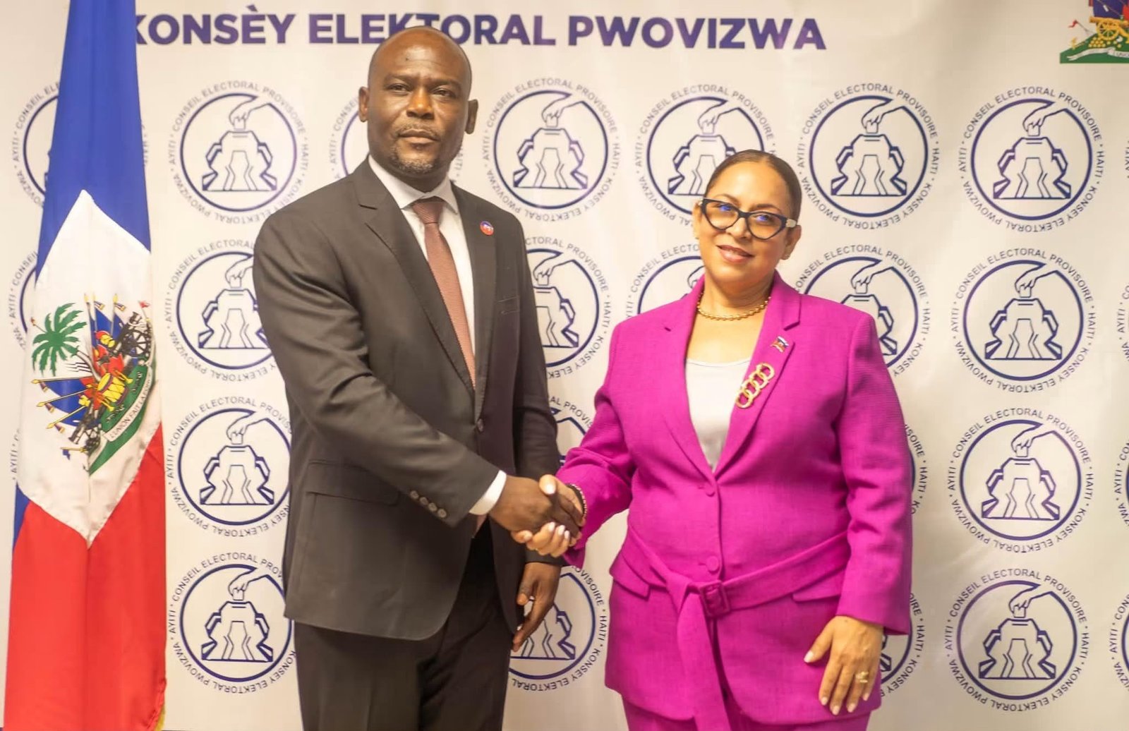 La ministre Raina Forbin, tailleur rose, serre la main d'un responsable du Conseil électoral provisoire devant un mur portant le logo du CEP répété en français et en créole, drapeau haïtien à gauche.