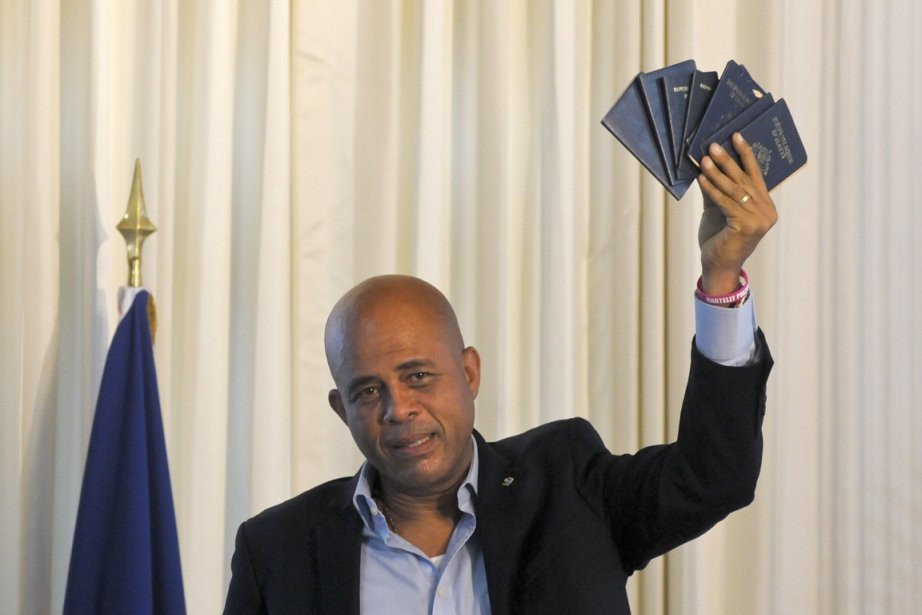 Michel Martelly brandissant plusieurs passeports haïtiens, souriant, devant un drapeau.