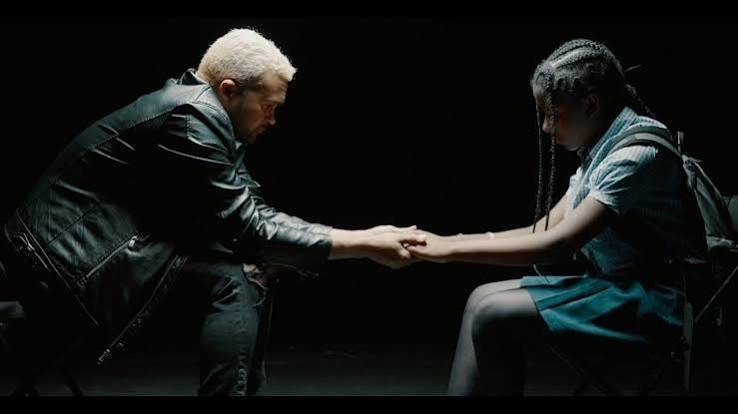 Scène tirée du clip vidéo évoquant le mot d'ordre « Èske nou pa moun ankò ? », un homme agenouillé tenant la main d'une jeune fille en tenue scolaire.