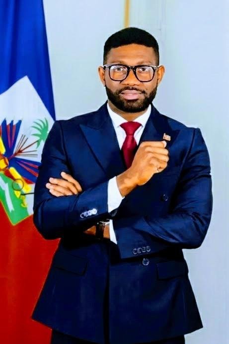 Wisner Laguerre, spécialiste en Relations internationales et Études diplomatiques, devant le drapeau haïtien.